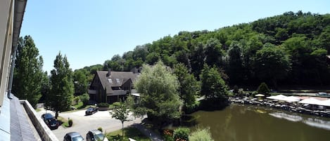 Vista al río con un edificio, coches aparcados y una zona de comedor con sombrillas.