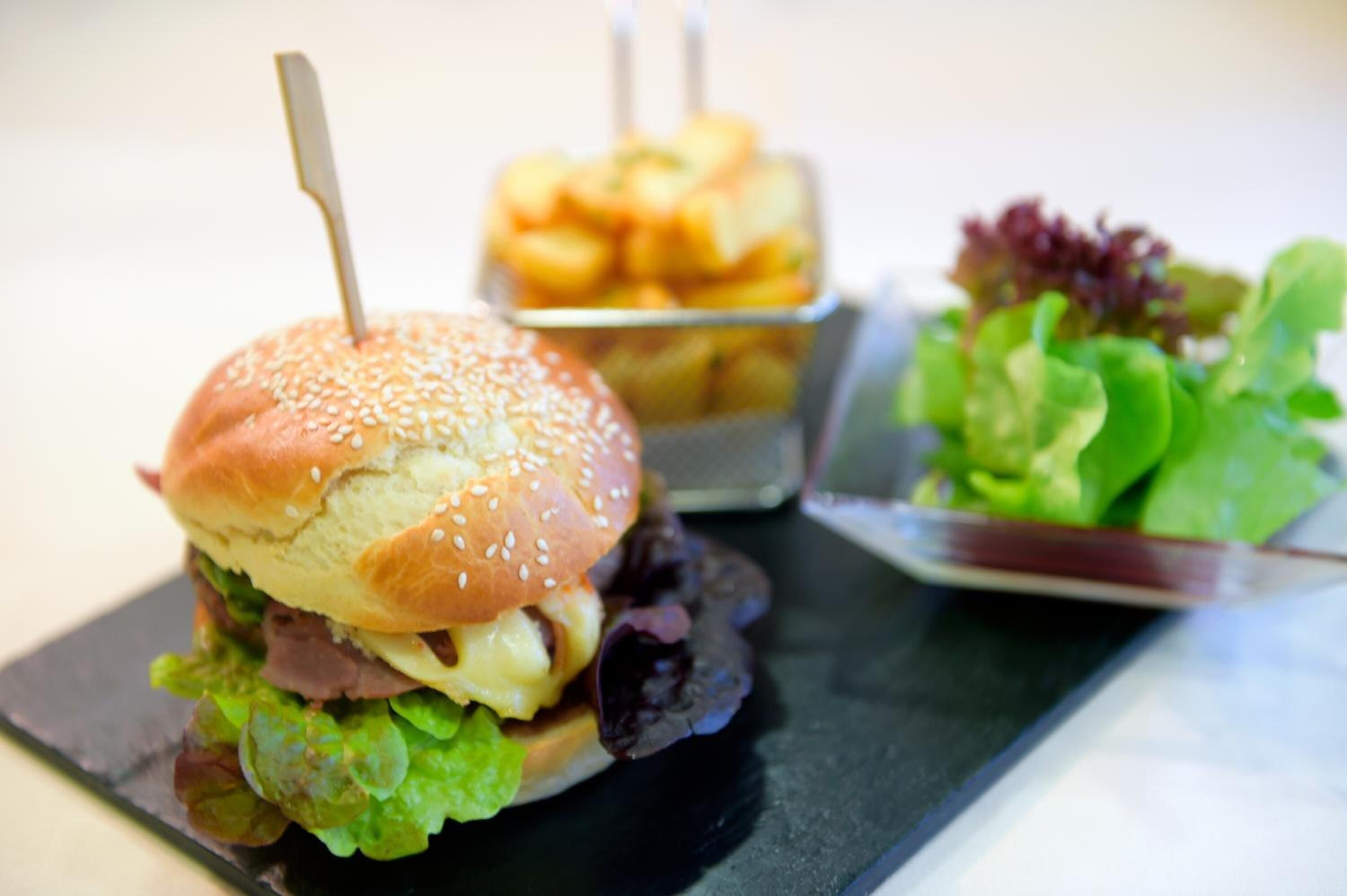 A sandwich with a toothpick, a container of fries, and a side salad on a black tray.