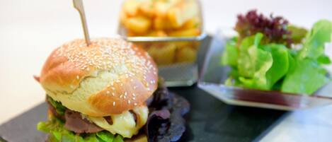 A sandwich with a toothpick, a container of fries, and a side salad on a black tray.
