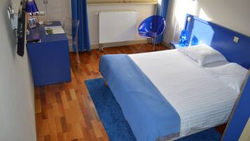 Habitación de hotel con cama, escritorio con lámpara, silla y ventana con cortinas.
