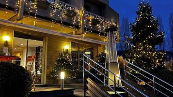 A modern building with a balcony decorated with string lights, a staircase, and Christmas trees.