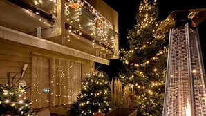 A modern building with a balcony adorned with string lights, outdoor seating, and a decorative tree. - Hôtel du Lac (Guebwiller)