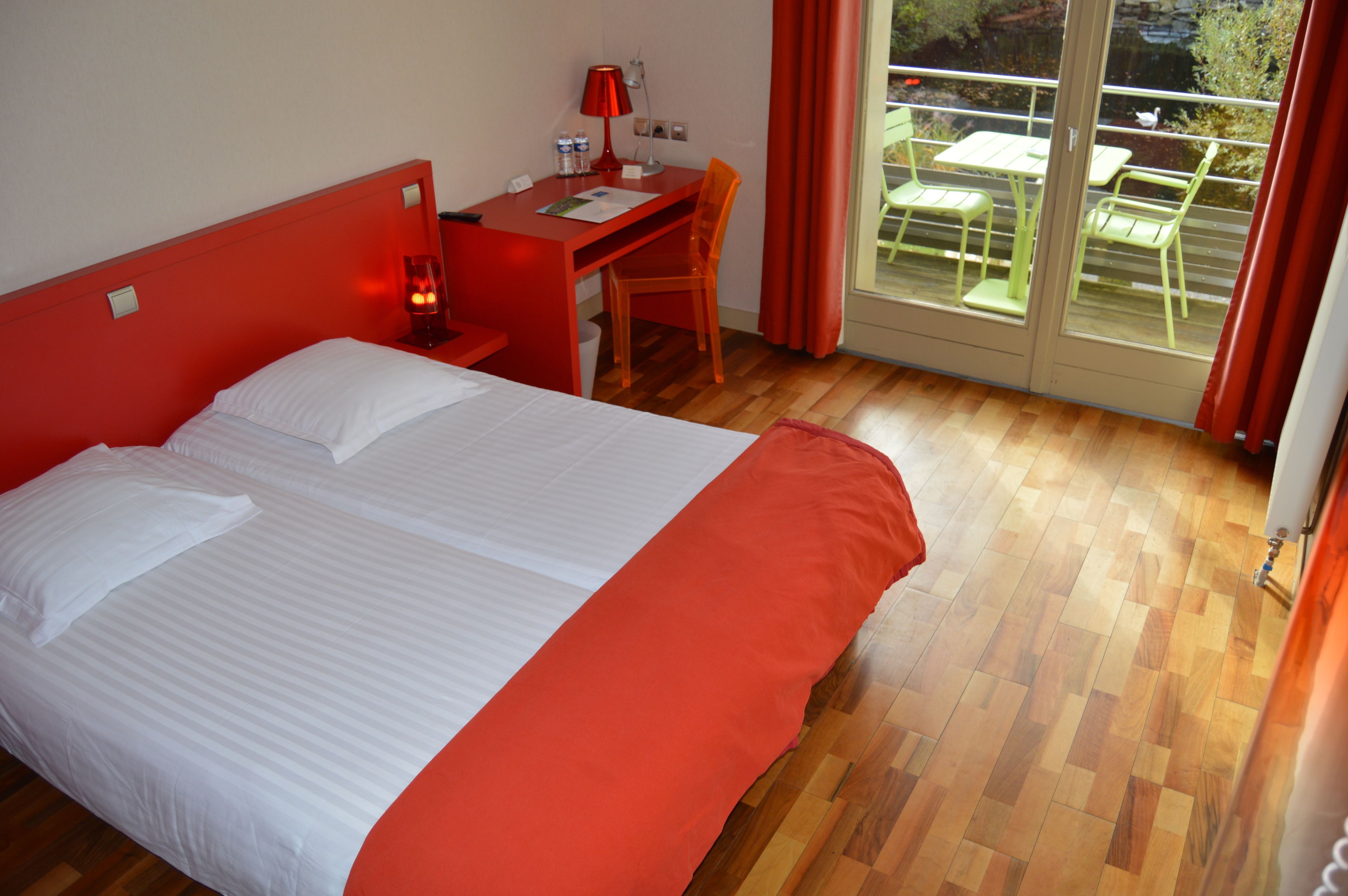 A hotel room with a bed, a desk, and a chair. There is a balcony with a table and chairs.