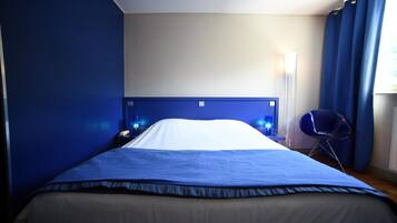 A hotel room with a large bed, a nightstand, a chair, and a window with curtains.