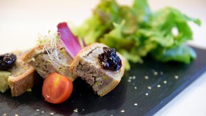 A close-up of a dish with a slice of meat, a tomato, and some greens on a black plate. - Hôtel du Lac (Guebwiller)