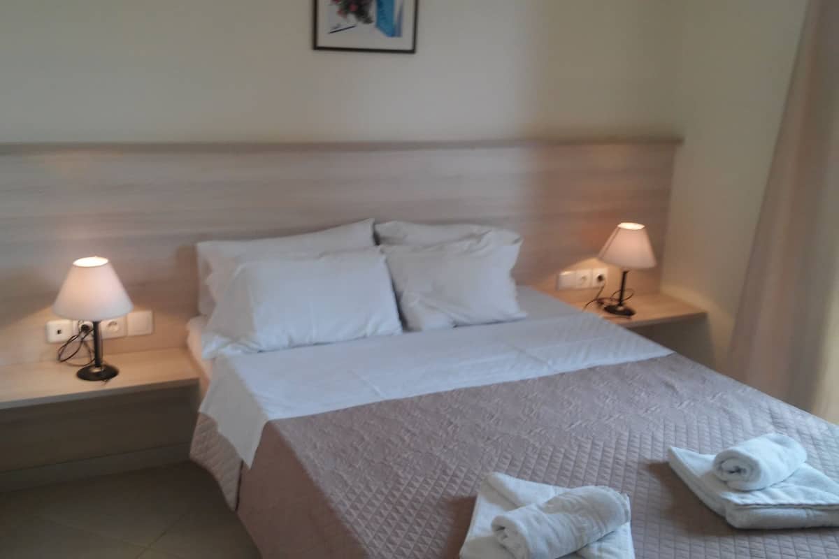 A hotel room with a bed, two bedside lamps, a nightstand, and a folded towel on the bed.