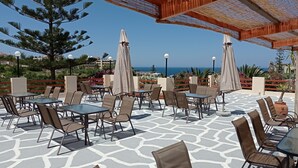 An outdoor patio with tables and chairs, a view of the sea, and a pergola structure. - Alexandros Studios (Chania)