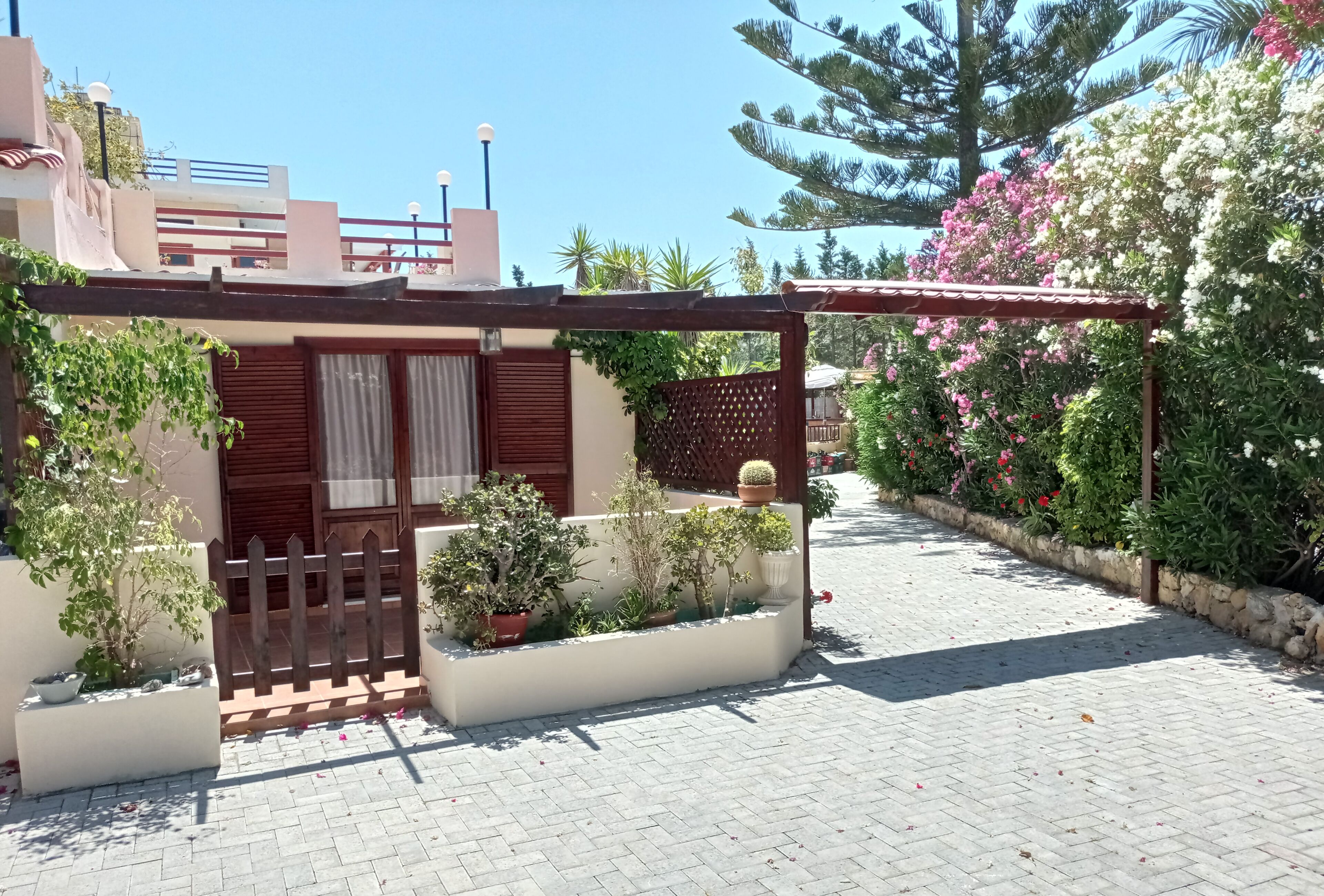 A residential building with a paved courtyard, potted plants, and a wooden gate.