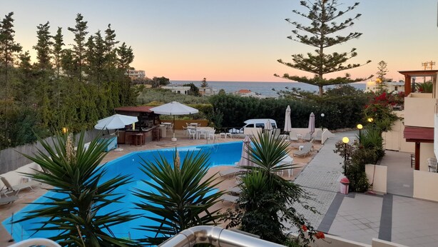 A poolside area with lounge chairs, umbrellas, and a view of the sea at sunset. - Alexandros Studios (Chania)