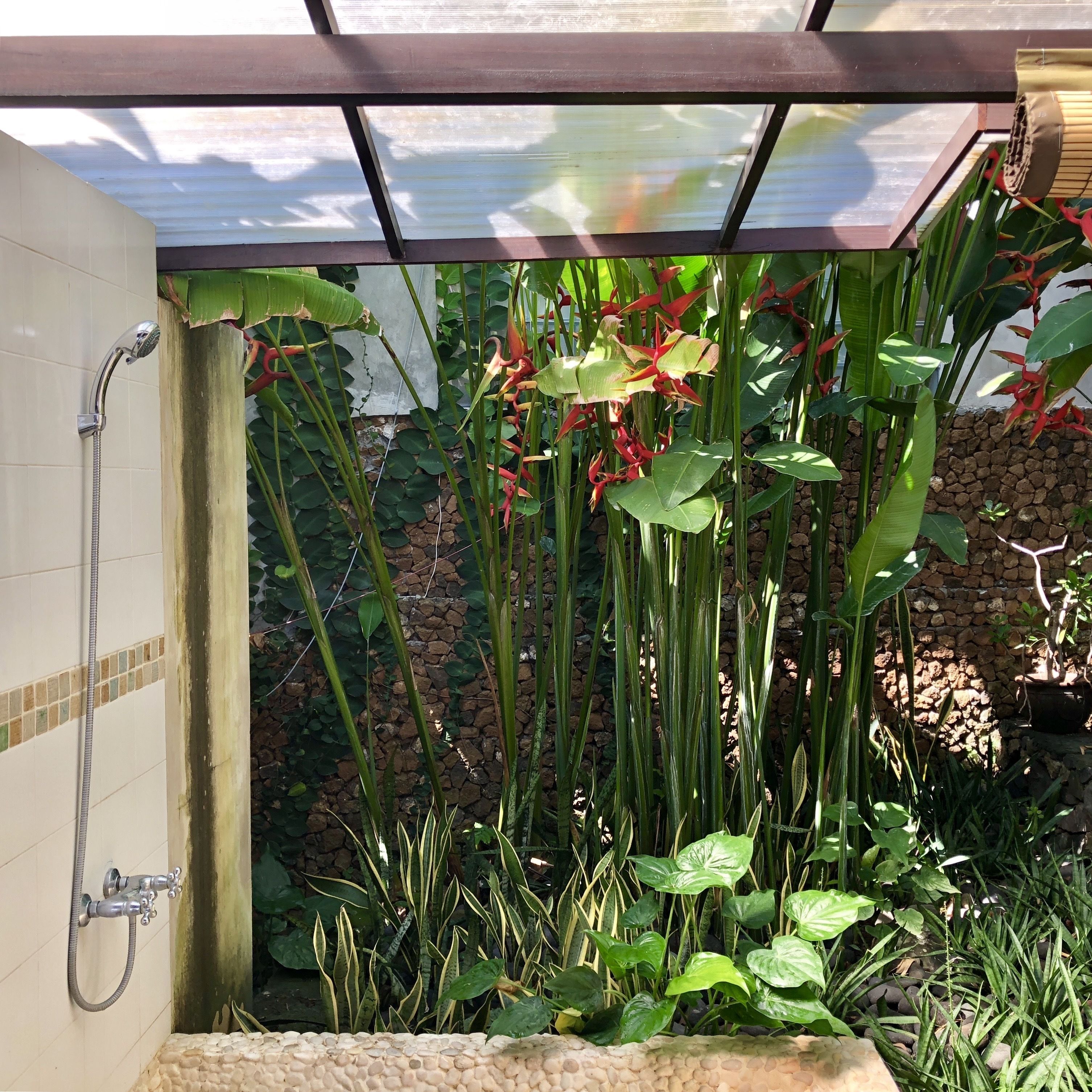 Zona de ducha con pared de azulejos, cabezal de ducha y manguera.