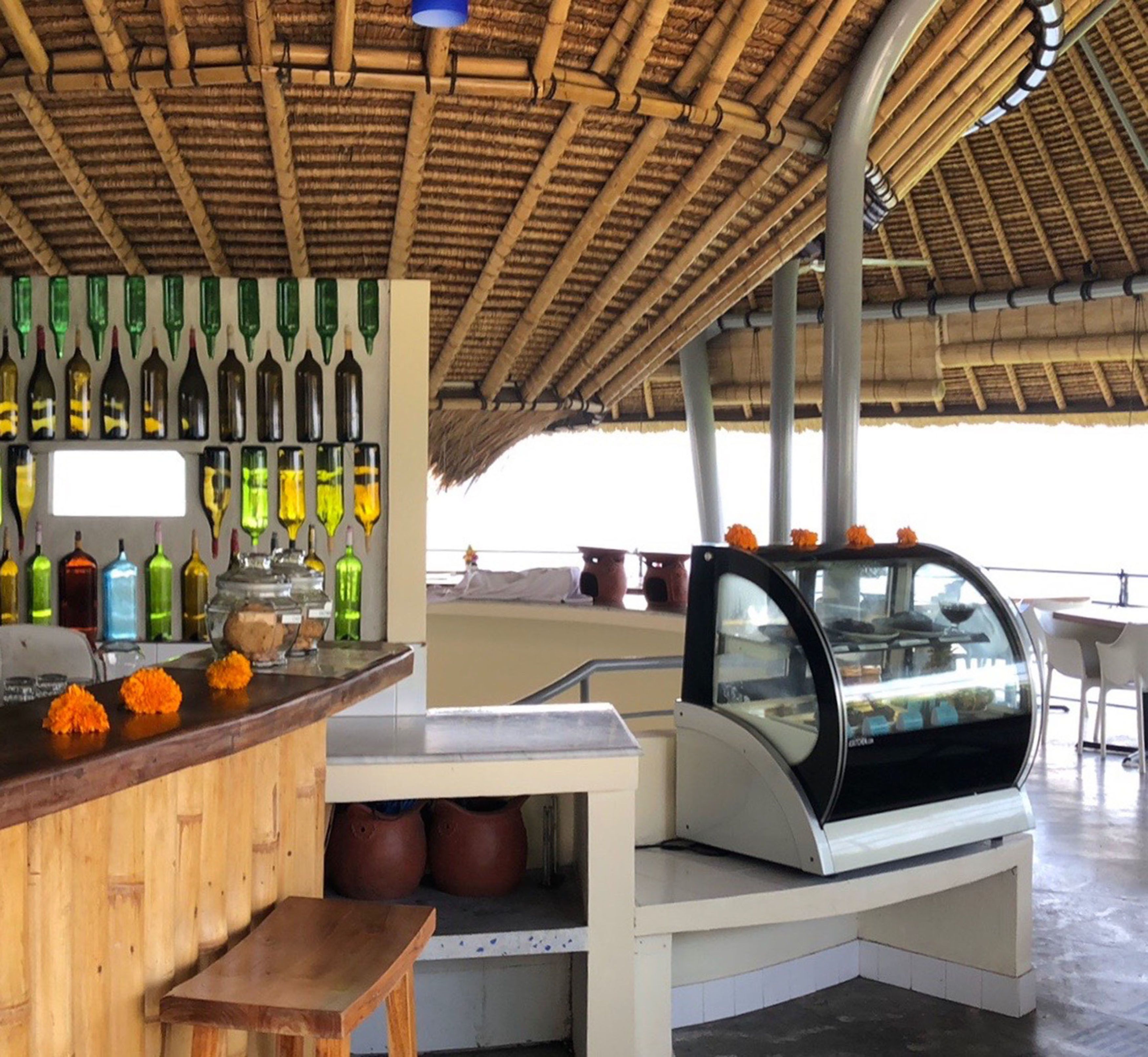 Eine Bar mit Bambusdecke, einer farbenfrohen Flaschenausstellung und einer Dessertvitrine.