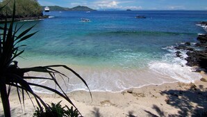 Una playa con agua cristalina, barcos y una isla a lo lejos.
