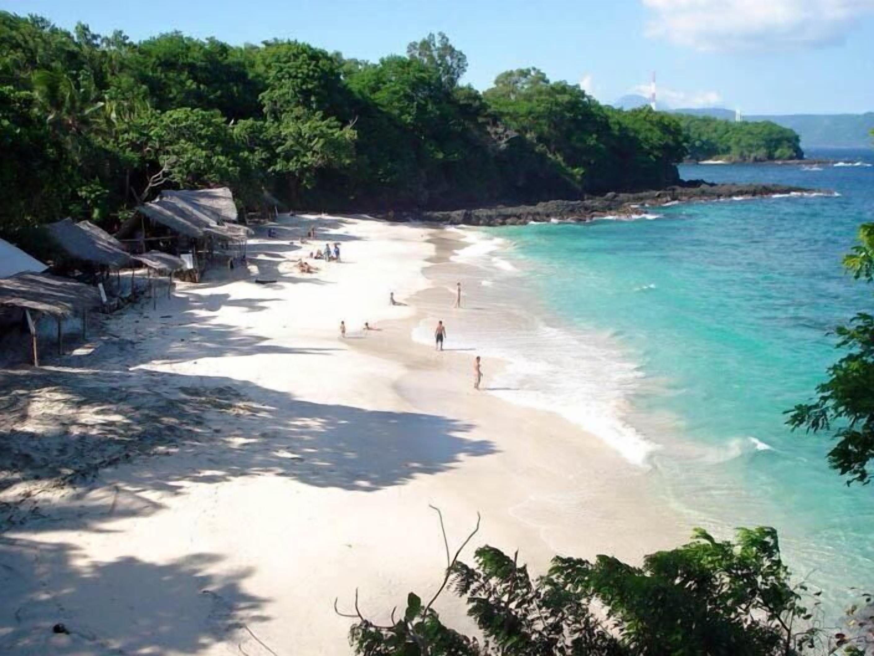 Una playa con agua turquesa cristalina, una orilla arenosa y cabañas con techo de paja.