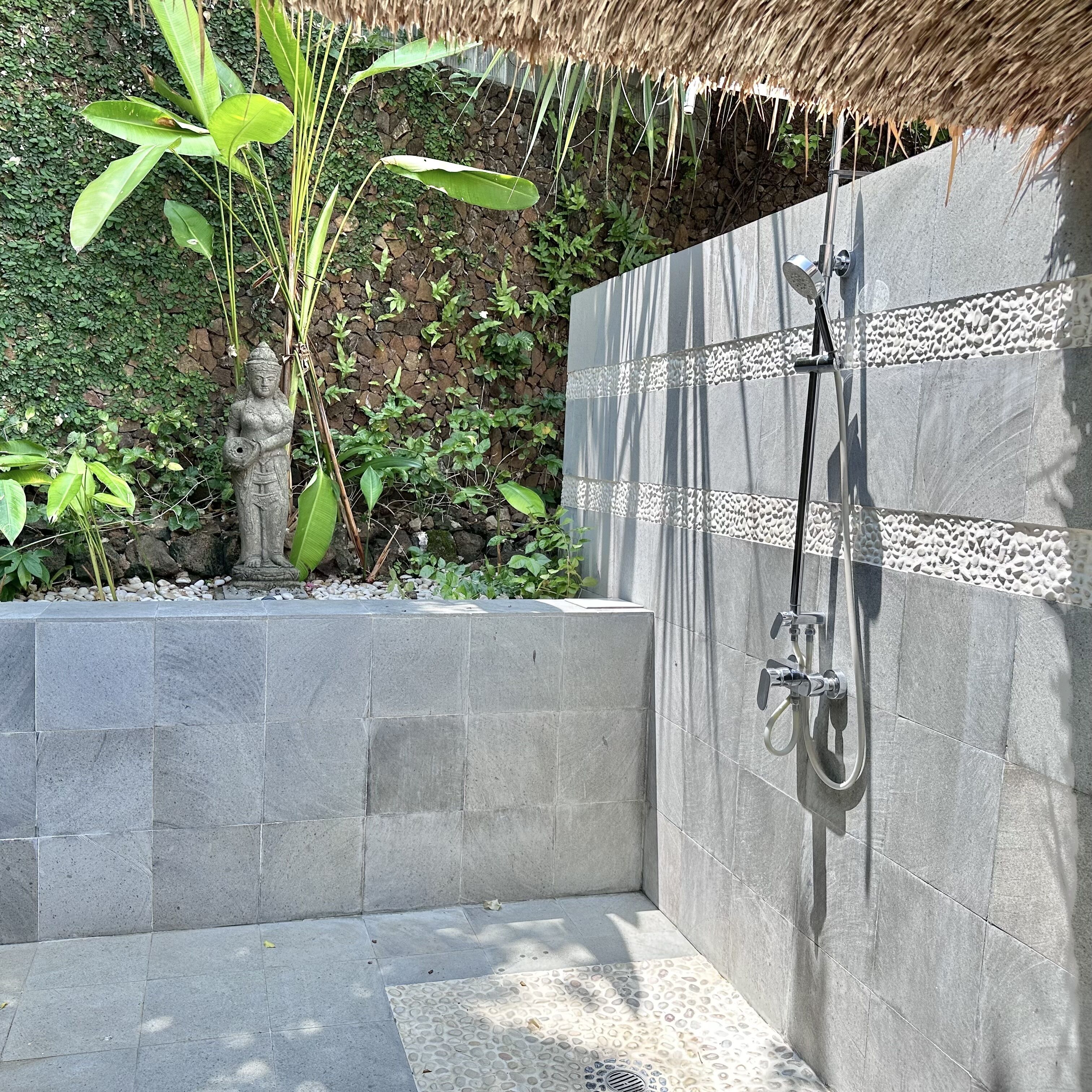 A modern shower area with a stone wall, a metal showerhead, and a thatched roof overhead.