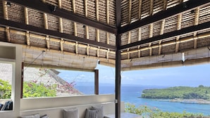Un área de estar exterior moderna con vista al océano y una estructura de techo de paja.