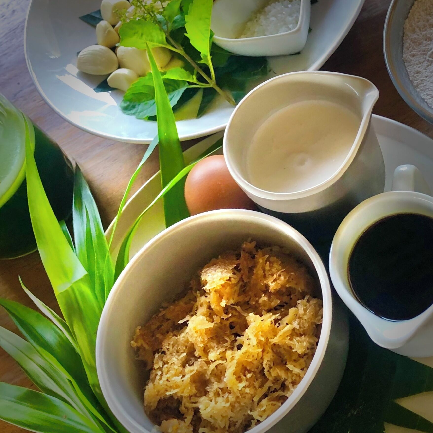 A table with a bowl of shredded food, a cup of coffee, a plate with eggs, and a pitcher of a white liquid.