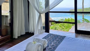 Un dormitorio con una cama grande, cortinas blancas y vista al océano.