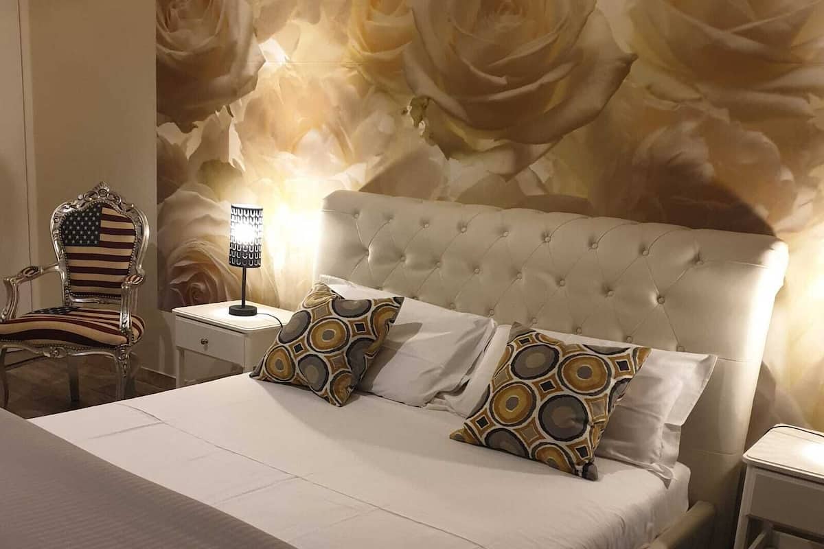 Quarto com uma cama grande, mesa de cabeceira, cadeira e parede com padrão floral.