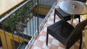 Ein Balkon mit kariertem Boden, Metallgeländer und Korbmöbeln.