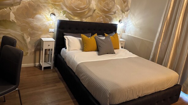 Ein Schlafzimmer mit einem großen Bett, einem Nachttisch, einem Sessel und einer Wand mit floralem Wandbild.