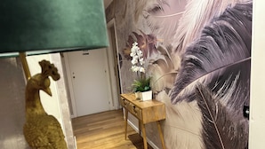 Ein Flur mit Holzboden, einer grünen Lampe, einem kleinen Holztisch mit einer Pflanze und einer Wand mit einem großen Feder-Wandgemälde.
