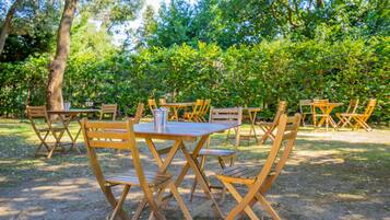 Un espace extérieur aménagé pour les repas, avec des tables et des chaises en bois, entouré d’arbres.
