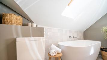 Un bagno moderno con una vasca freestanding, un water e un piccolo sgabello con asciugamani.