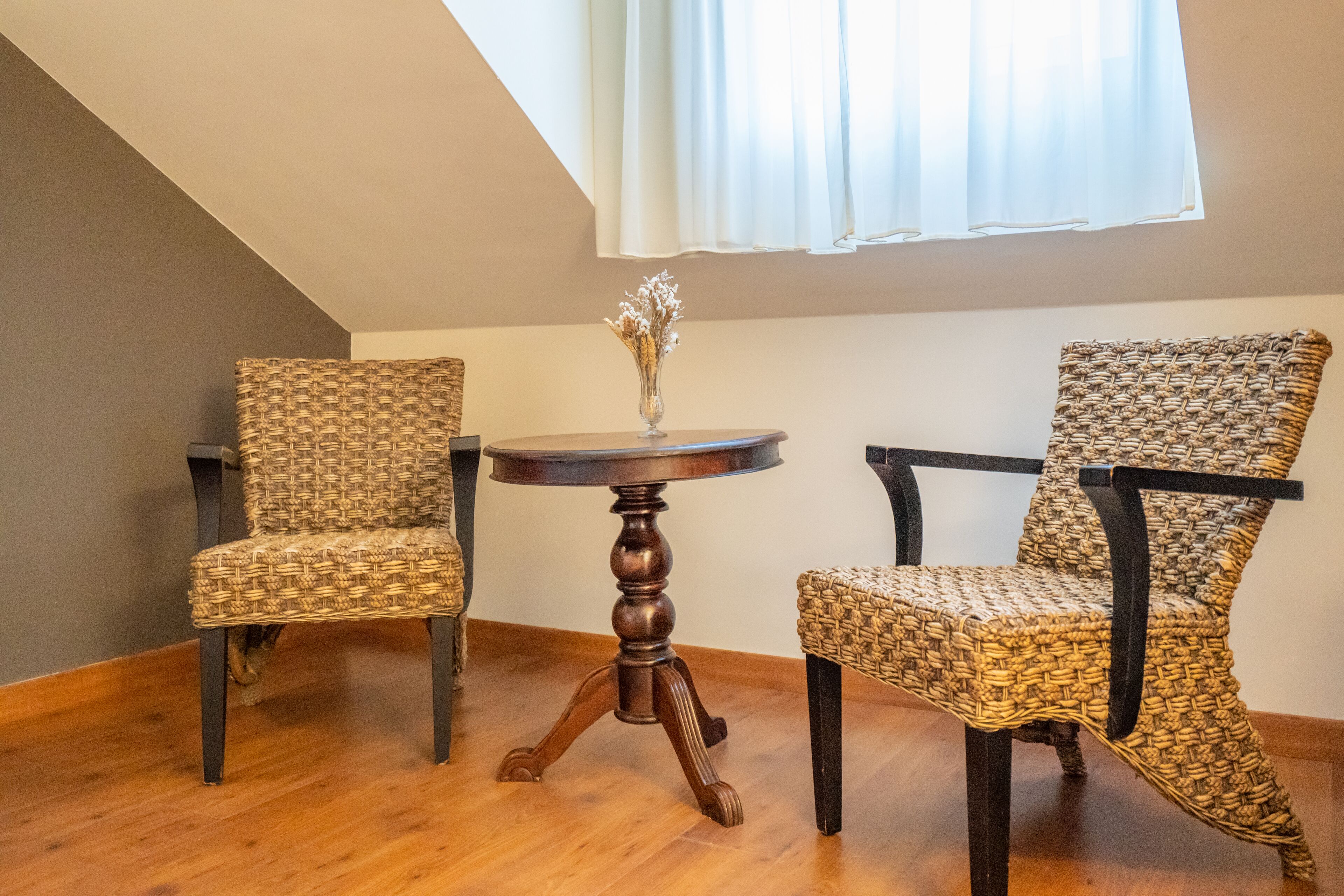Une pièce comprenant deux fauteuils en osier, une table ronde en bois et un vase contenant des fleurs séchées.