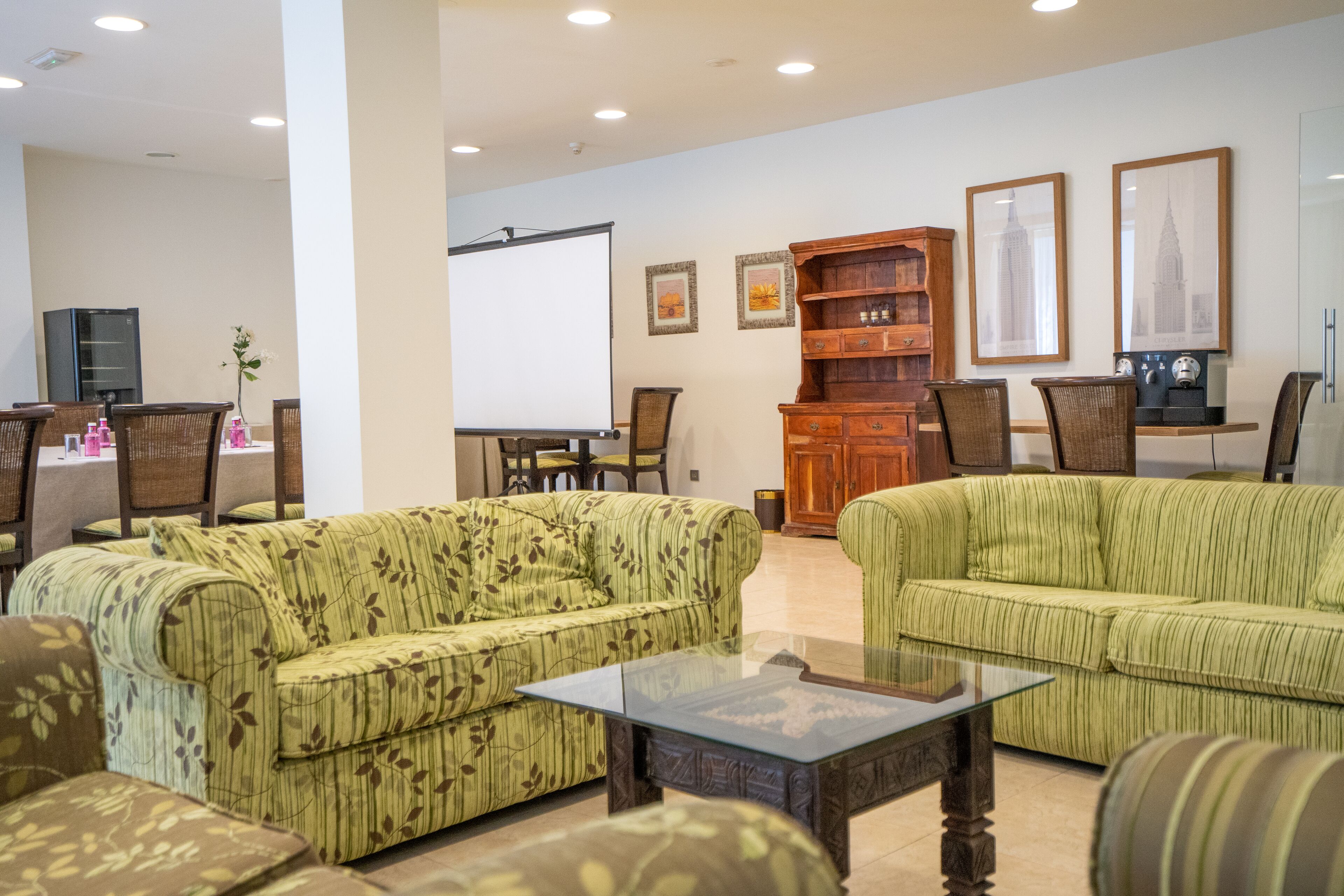 A living room with green-striped sofas, a glass coffee table, a wooden cabinet, and framed pictures on the wall.