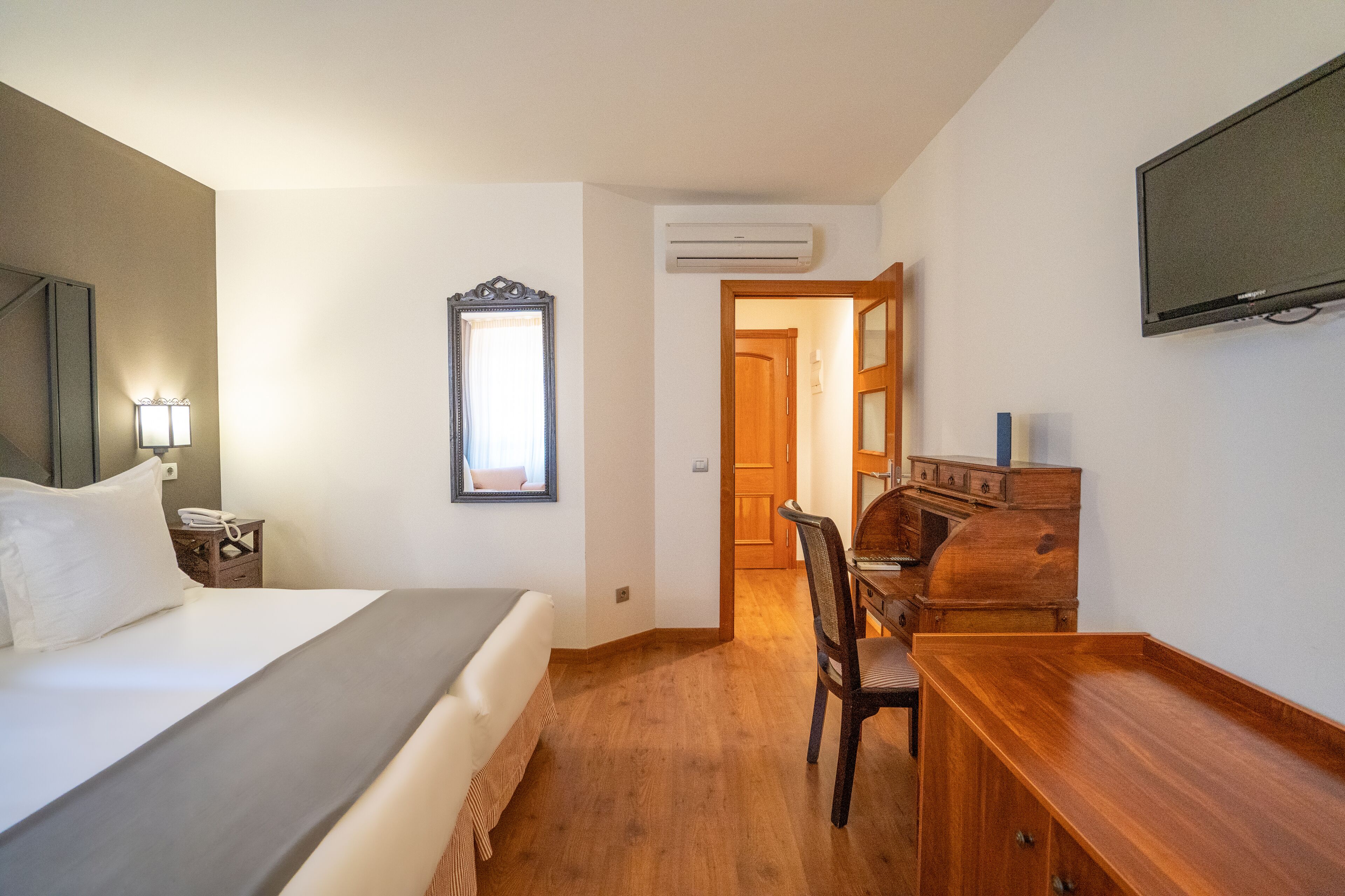 Habitación de hotel con cama, escritorio, silla, cómoda, televisor y aire acondicionado.
