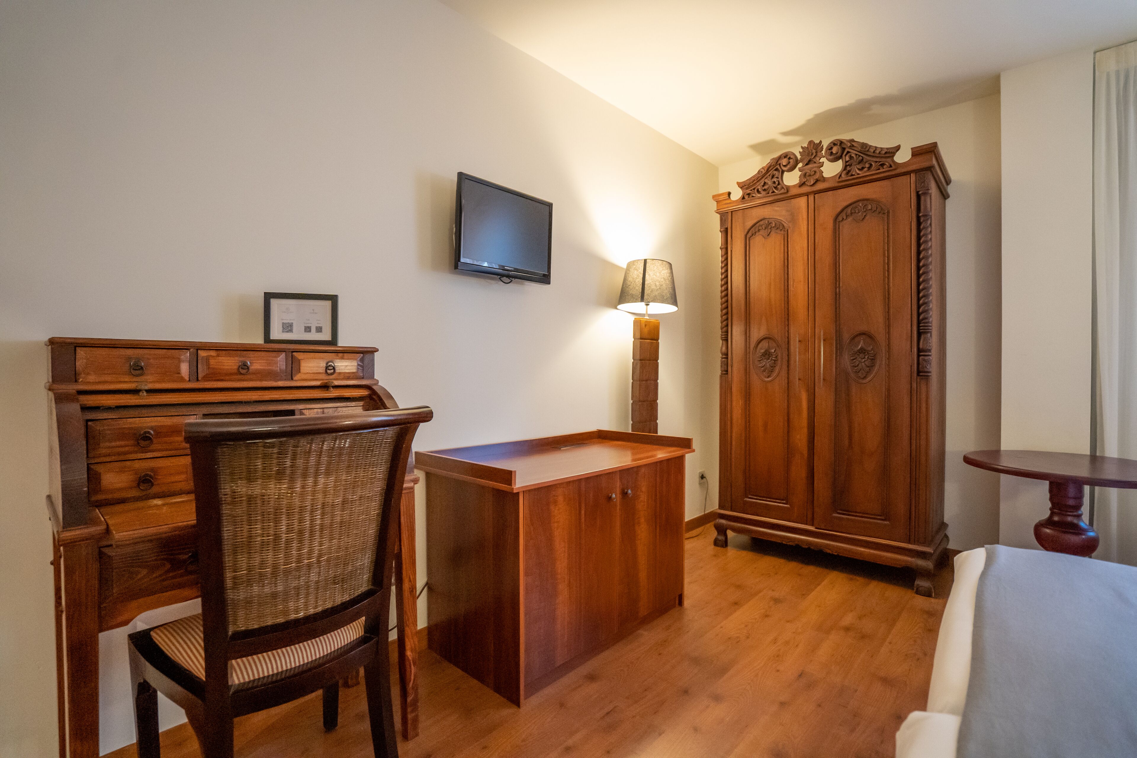 Habitació amb escriptori de fusta, cadira, armari i televisió penjada a la paret.