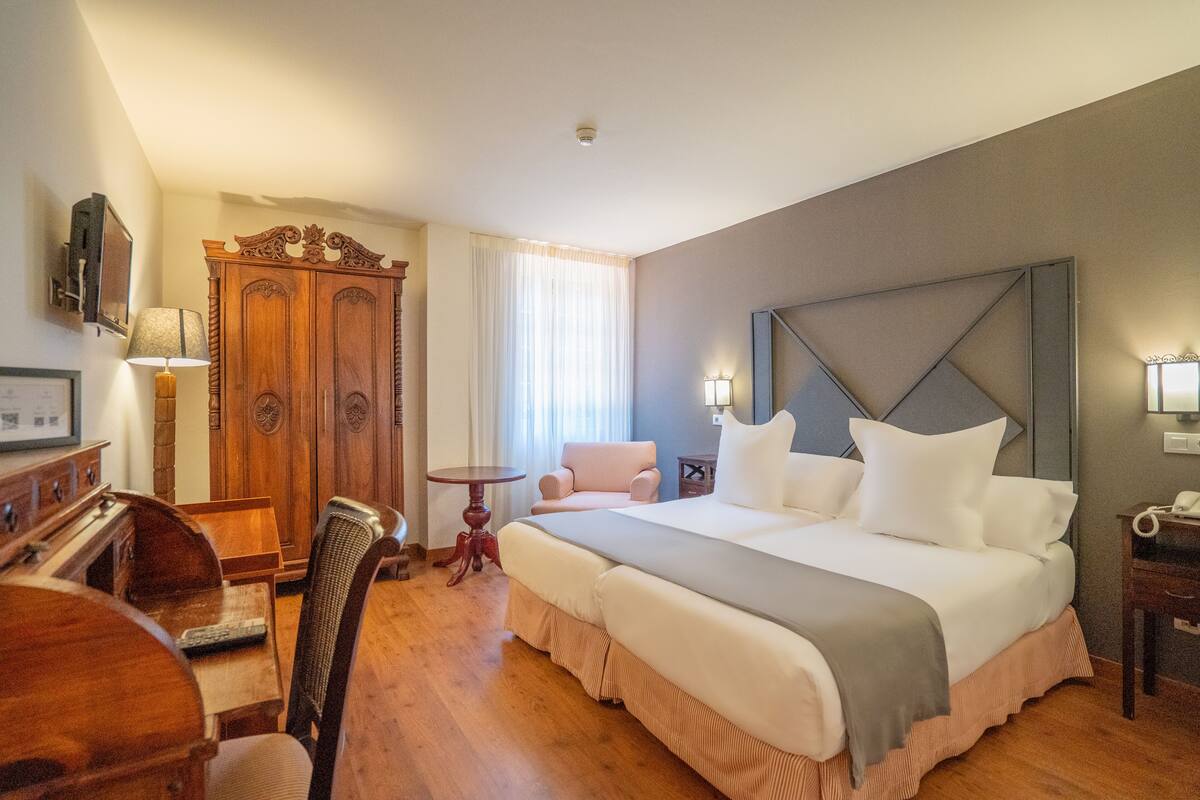 A hotel room with a large bed, wooden furniture, a desk, and a chair.