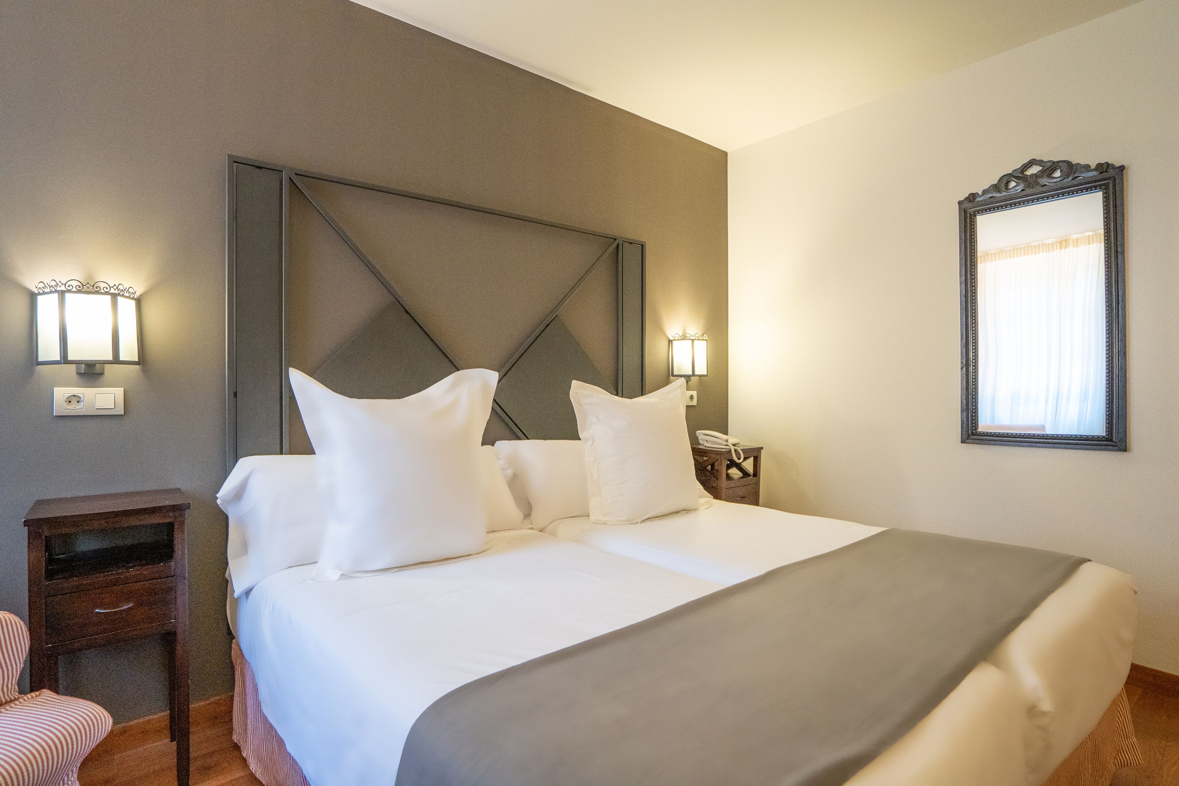 A hotel room with a large bed, two bedside tables, a nightstand, and a mirror on the wall.