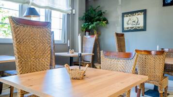 Un coin repas avec une table en bois et des chaises en osier, une plante en pot et un tableau encadré au mur.