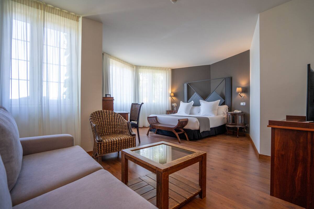 A hotel room with a bed, a sofa, a chair, a small table, and a TV.