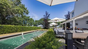A pool area with a fountain, outdoor seating, and umbrellas. - Fletcher Hotel Het Witte Huis (Soest)
