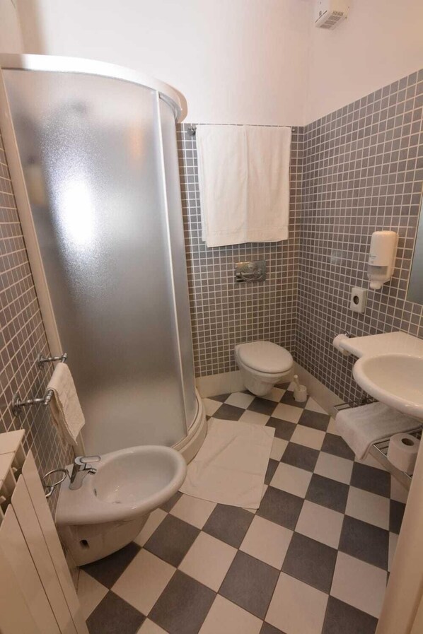 A bathroom with a shower, toilet, and sink, featuring a checkered floor and tiled walls.