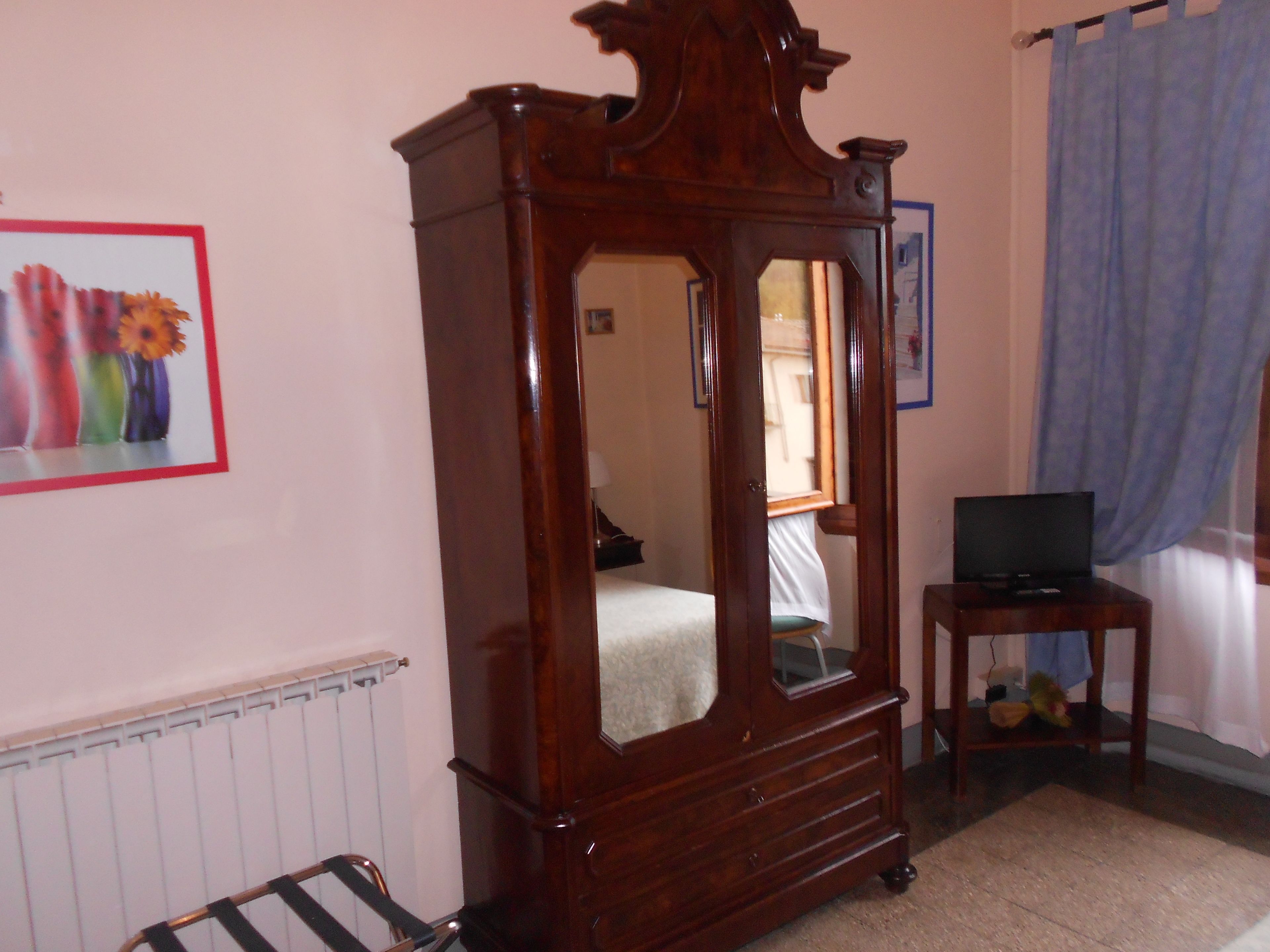 A bedroom with a wooden four-poster bed, a small bedside table with a television, and a radiator.
