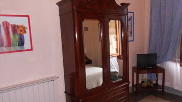 A bedroom with a wooden four-poster bed, a small bedside table with a television, and a radiator.