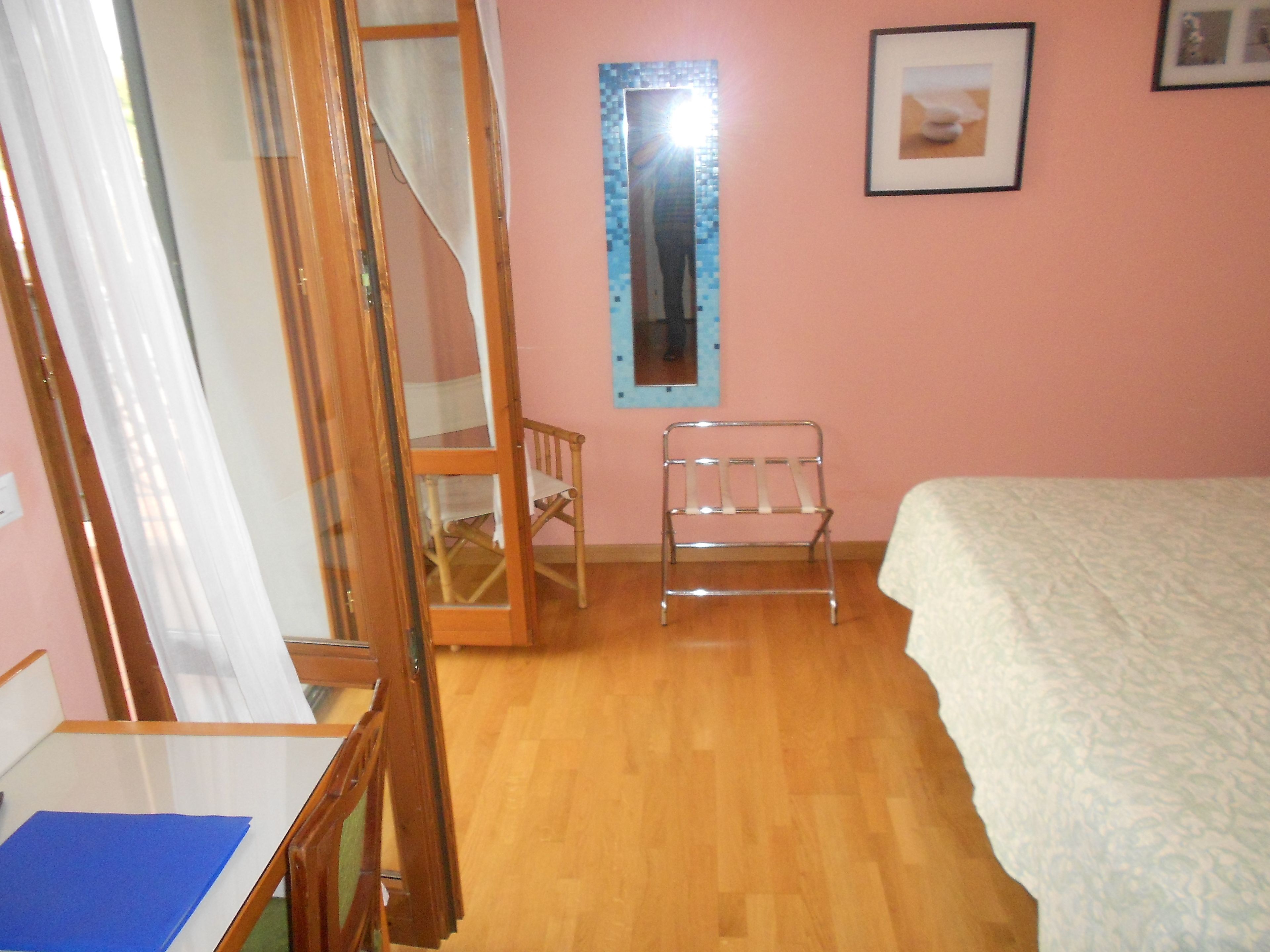 A bedroom with a wooden floor, a bed, a chair, a small table, and a mirror on the wall.
