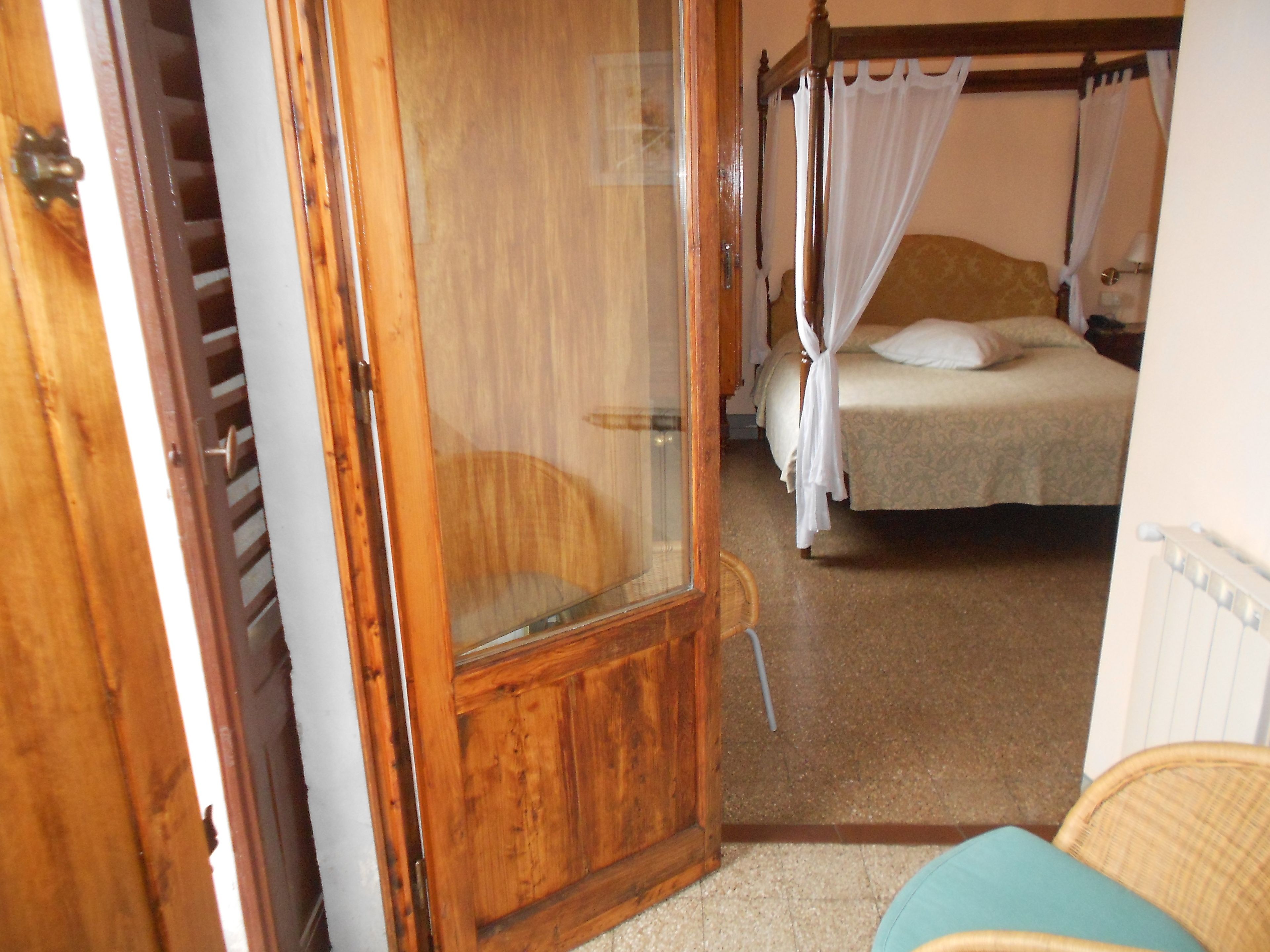 Un dormitorio con un armario de madera, una cama con dosel y una silla de mimbre.