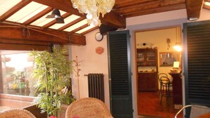 A cozy room with wicker furniture, a potted plant, and a view of the kitchen through open shutters.
