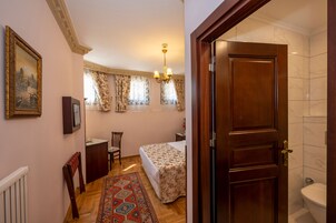 Ein Hotelzimmer mit einem Bett, einem Schreibtisch, einem Sessel, einem Fernseher, einer Chandelüster und einer Tür zu einem Badezimmer.