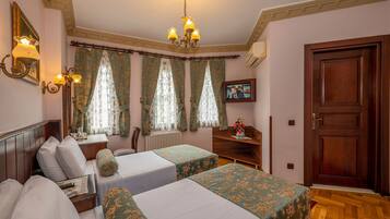 A hotel room with two beds, a wooden headboard, a small table with a lamp, a TV, and a door.
