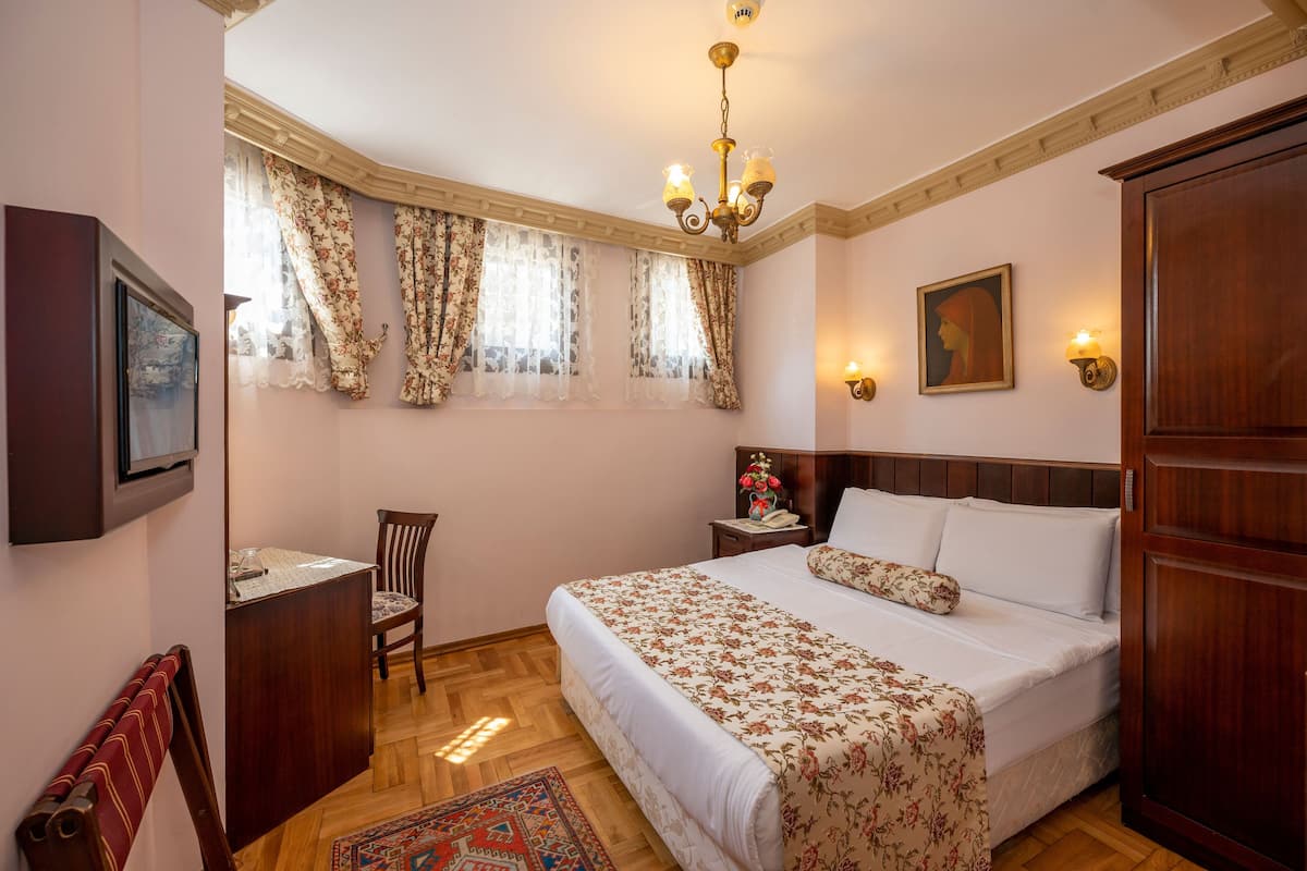 A bedroom with a bed, a desk, a chair, a nightstand, and a chandelier.