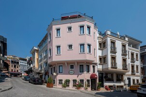 Un edificio a più piani con facciata rosa, diversi balconi e un ingresso a livello strada con piante in vaso.