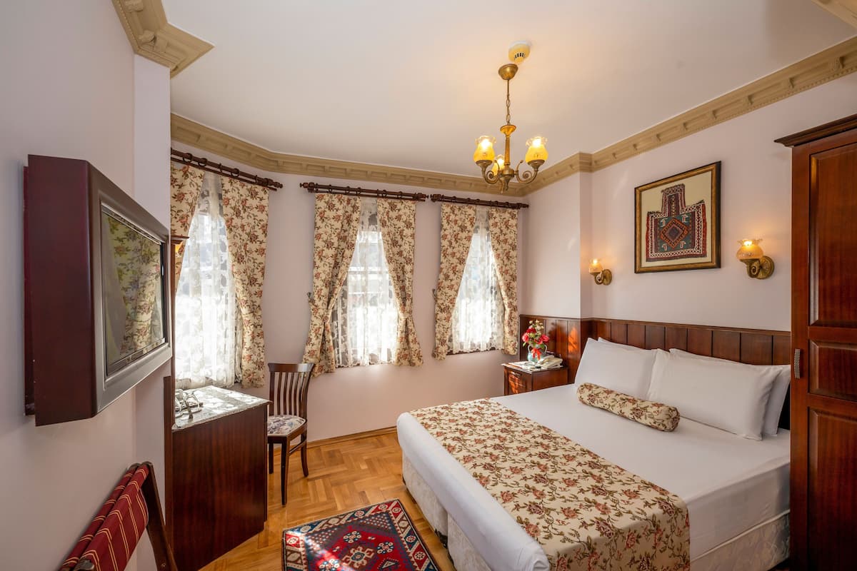 A bedroom with a large bed, a wooden headboard, a chandelier, and floral curtains.