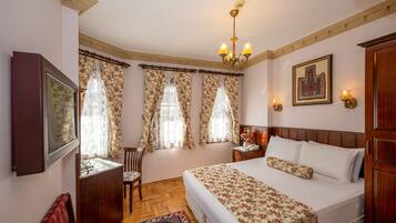 A bedroom with a large bed, a wooden headboard, a chandelier, and floral curtains.