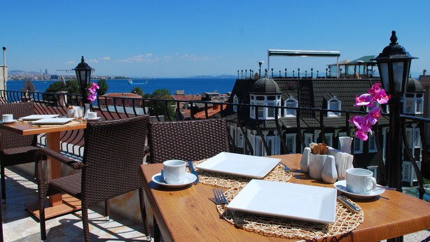 A terrace with dining tables set for two, equipped with white plates, cups, and cutlery.