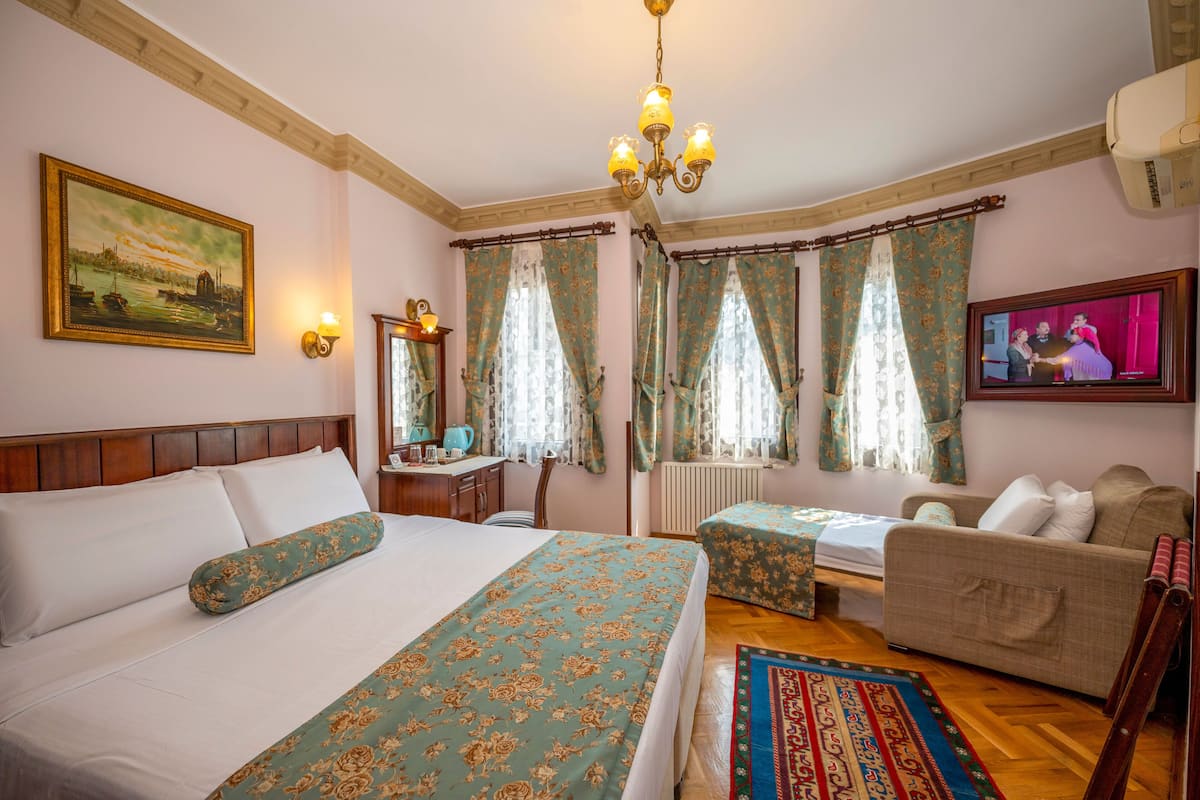 A hotel room with a bed, a sofa, a TV, and a painting on the wall.